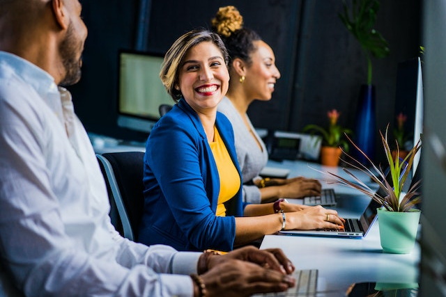 A woman smiles at her colleague while working on a laptop computer