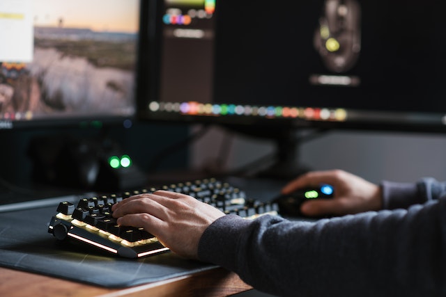 A computer user sits with one hand on the keyboard and one on the mouse.