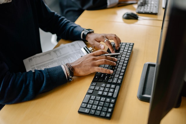 Person typing on a keyboard using data from a clipboard