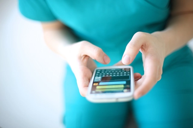 Healthcare provider wearing scrubs using a messaging app like WhatsApp on a smartphone